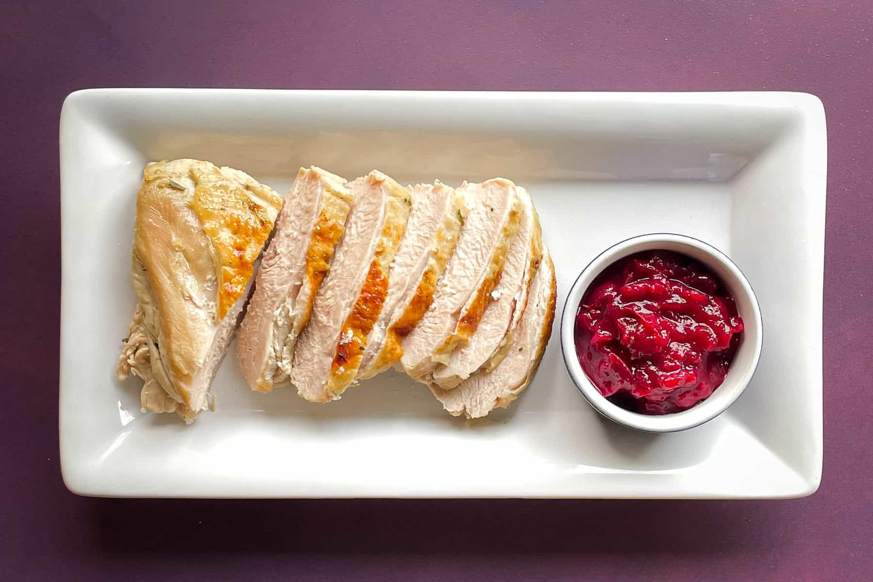 slices of browned turkey breast on a white plate with cranberry sauce.