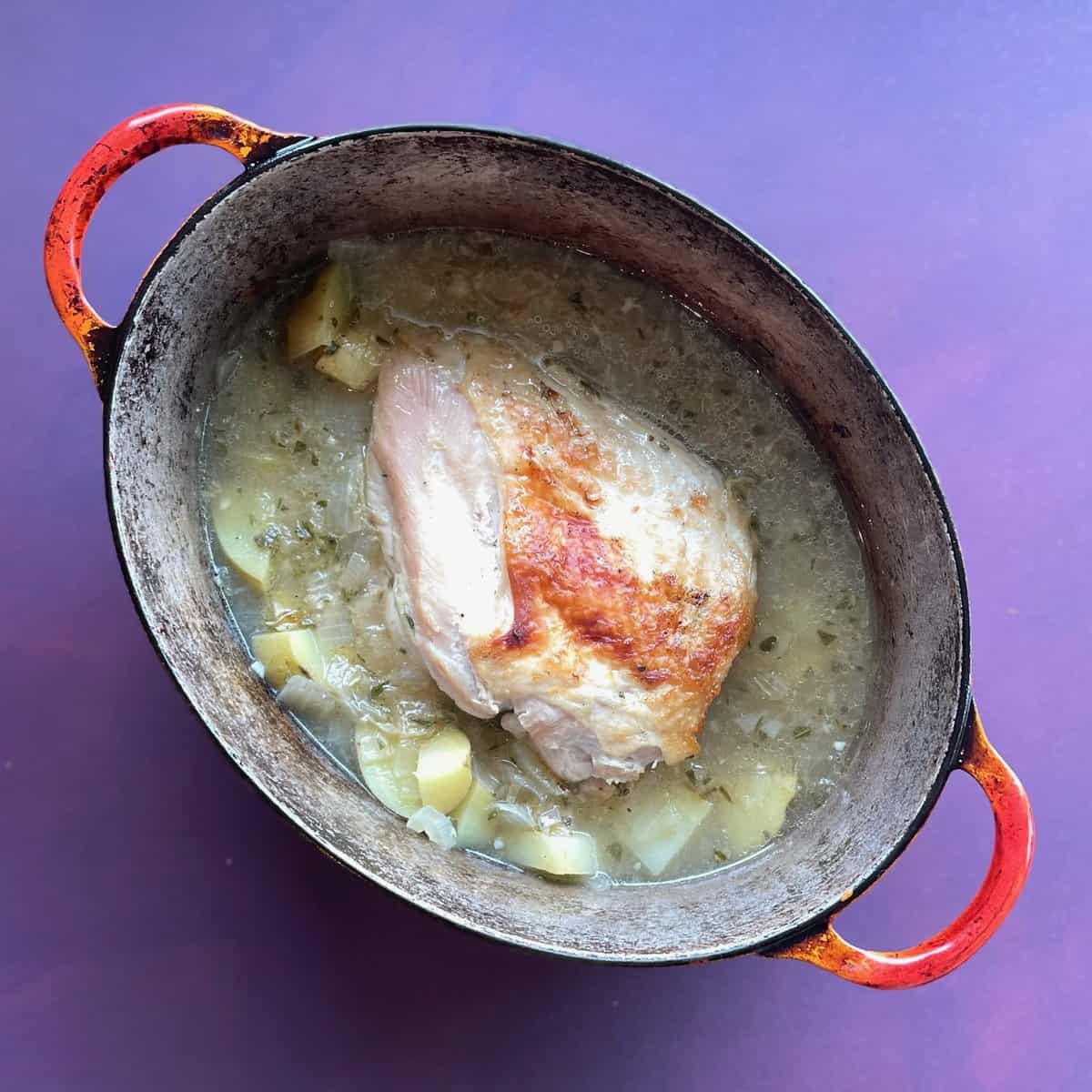 turkey breast in a Dutch oven surrounded by onions and potatoes and liquid.