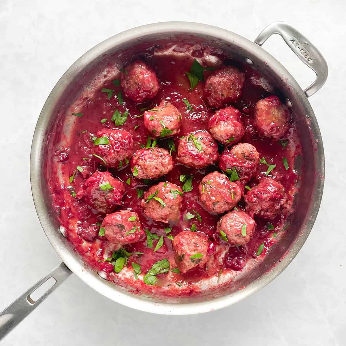 meatballs in cranberry sauce sprinkled with parsley in a skillet.