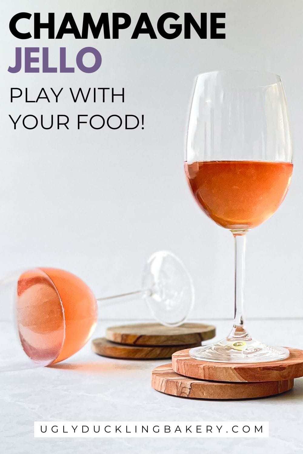 rose champagne jello in two wine glasses. One glass is upright on two coasters and the second is tipped over but the wine jello is not spilling out. The title says Champagne jello. Play with your food. And the website ugly duckling bakery dot com is at the bottom.