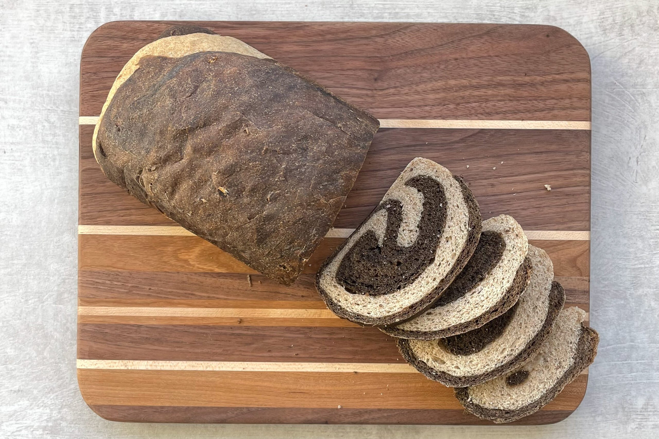 loaf of marble rye bread with four slices on a multi-colored wood cutting board.