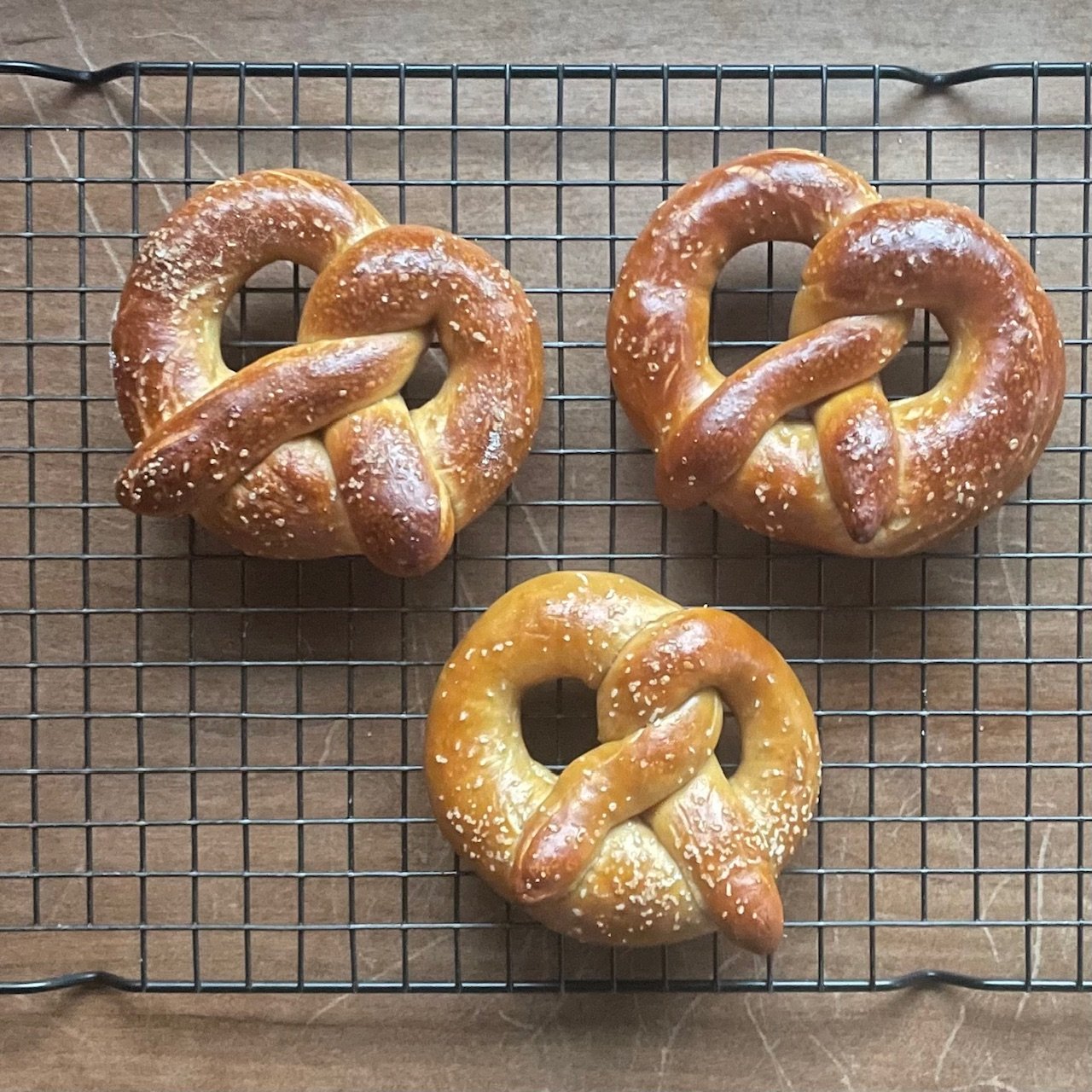 two sourdough discard pretzels made with food grade lye on a cooling rack compared to a lighter sourdough soft pretzel made with baking soda.