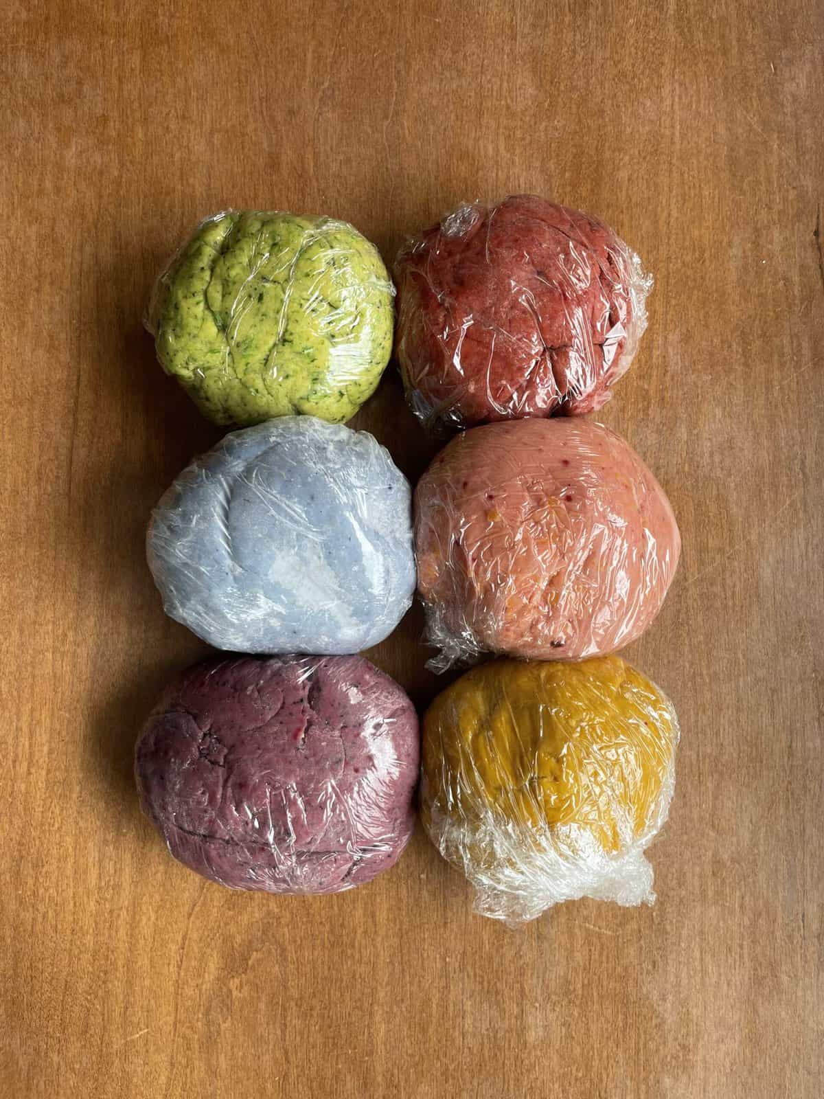 six batches of rainbow pasta dough wrapped in plastic.