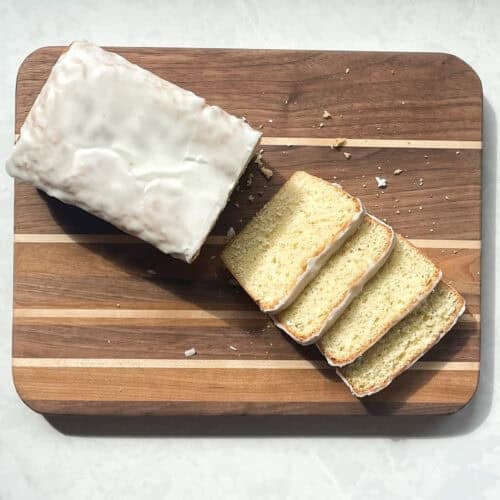 loaf cake with lime drizzle cut into four pieces on a cutting board.