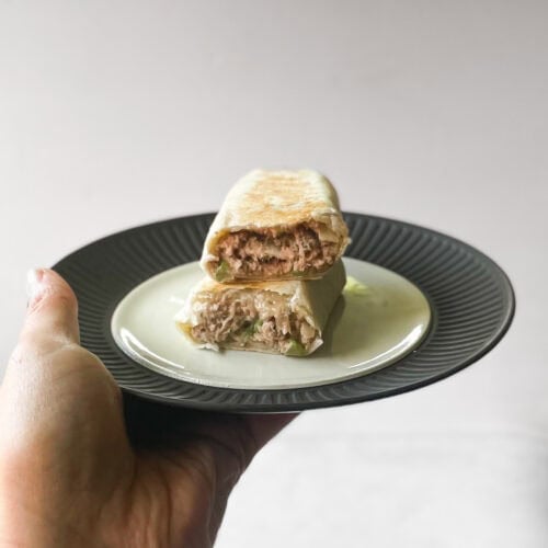 hand holding plate with tuna melt wrap cut in two with one half on the other.