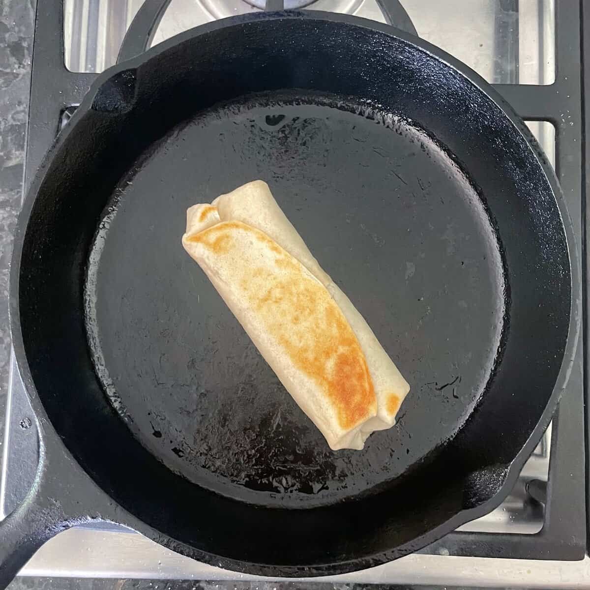browned seam side of a tuna melt wrap in a cast iron skillet.