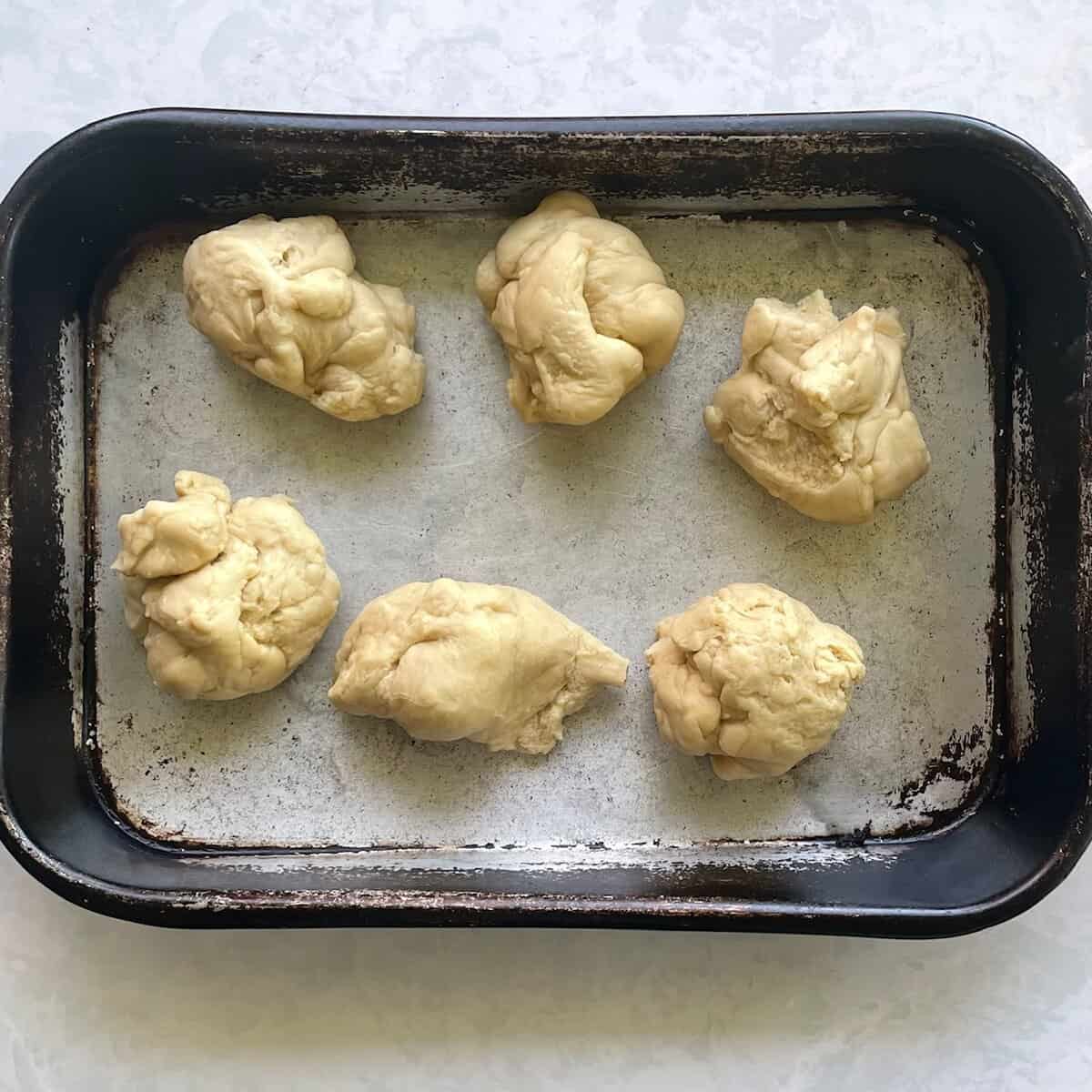 six balls of bread dough in a roasting pan.