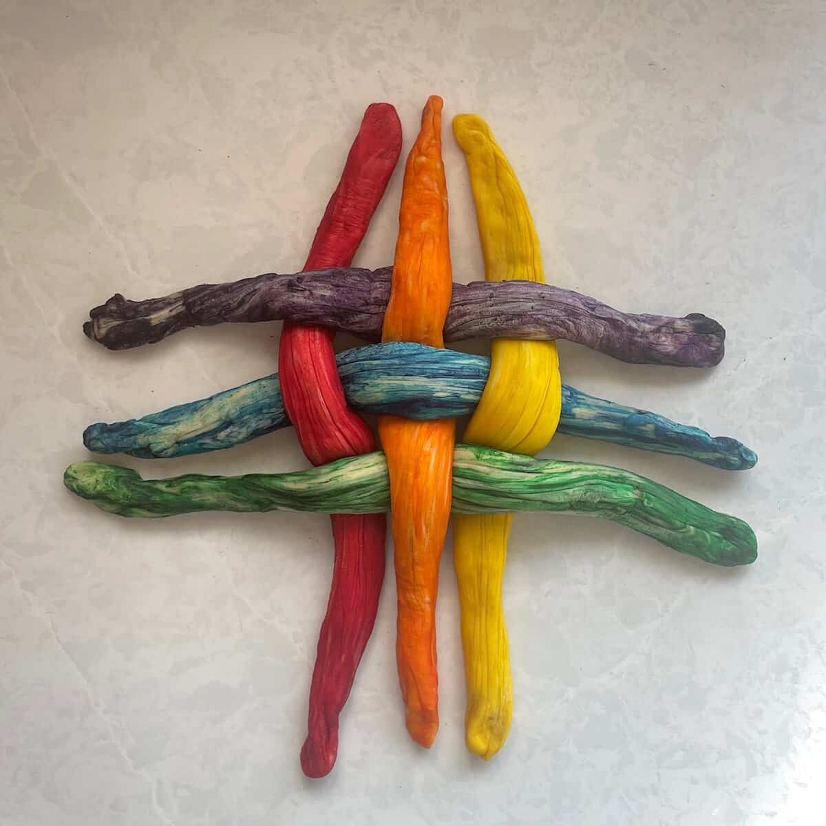 six rainbow challah strands in a basketweave pattern.