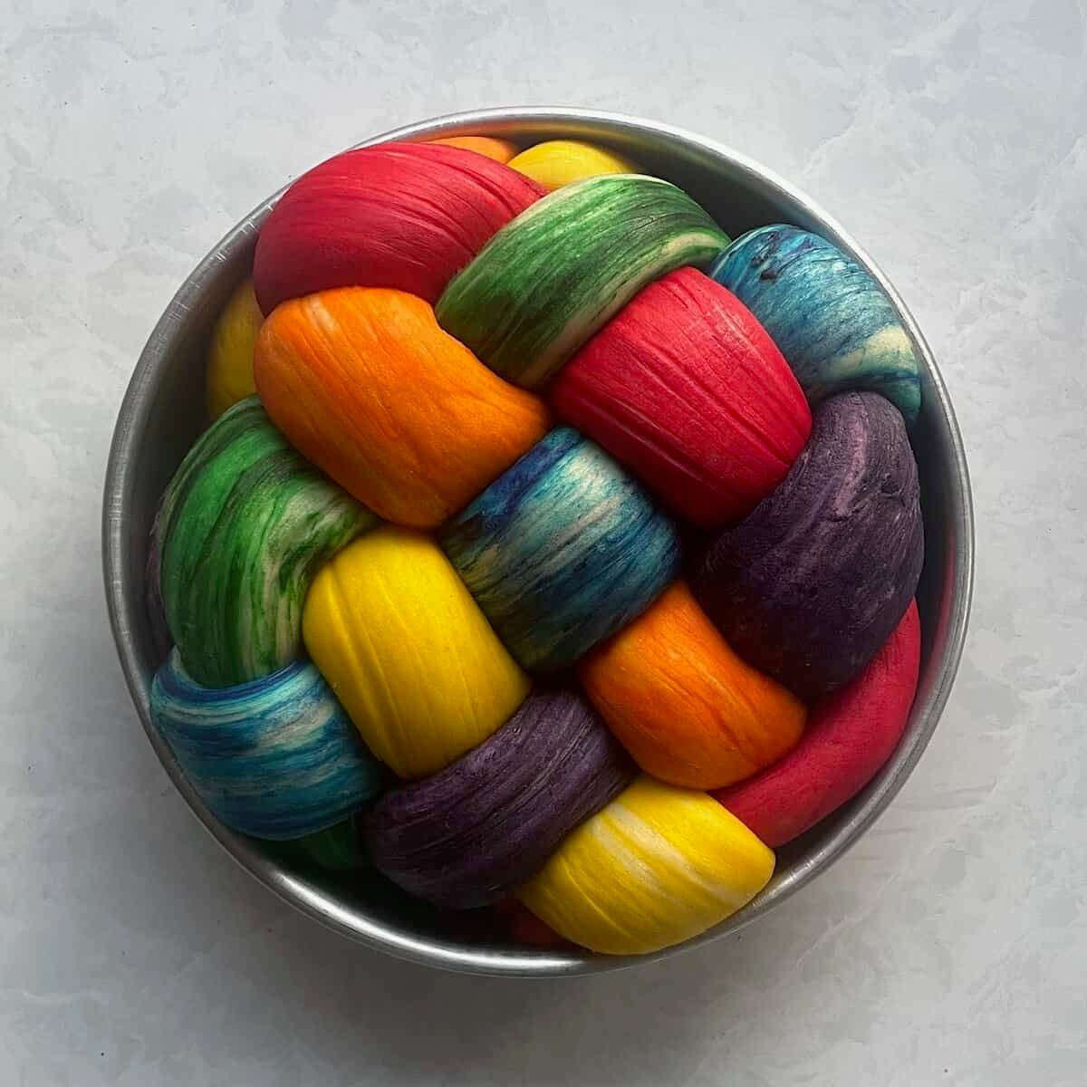round rainbow challah in a round cake pan ready for baking.