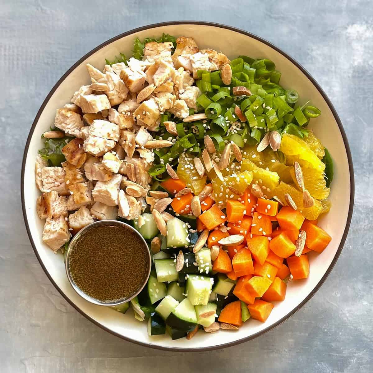 chopped chicken salad bowl with cucumber, carrot, orange, green onions, almonds, and sesame seeds.