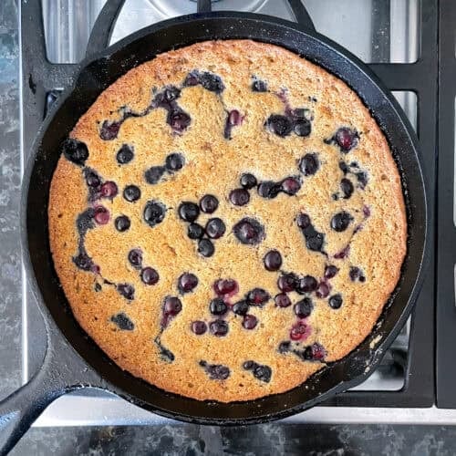 blueberry cake dotted with blueberries in a cast iron skillet on the stove.