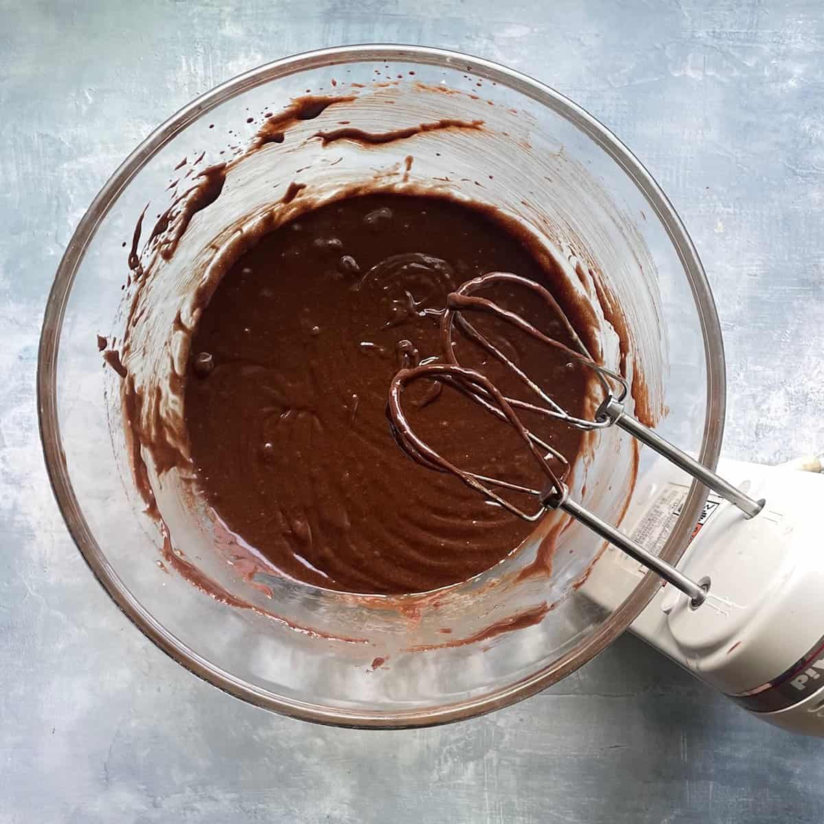 chocolate batter in a large glass bowl dripping off handheld beaters.