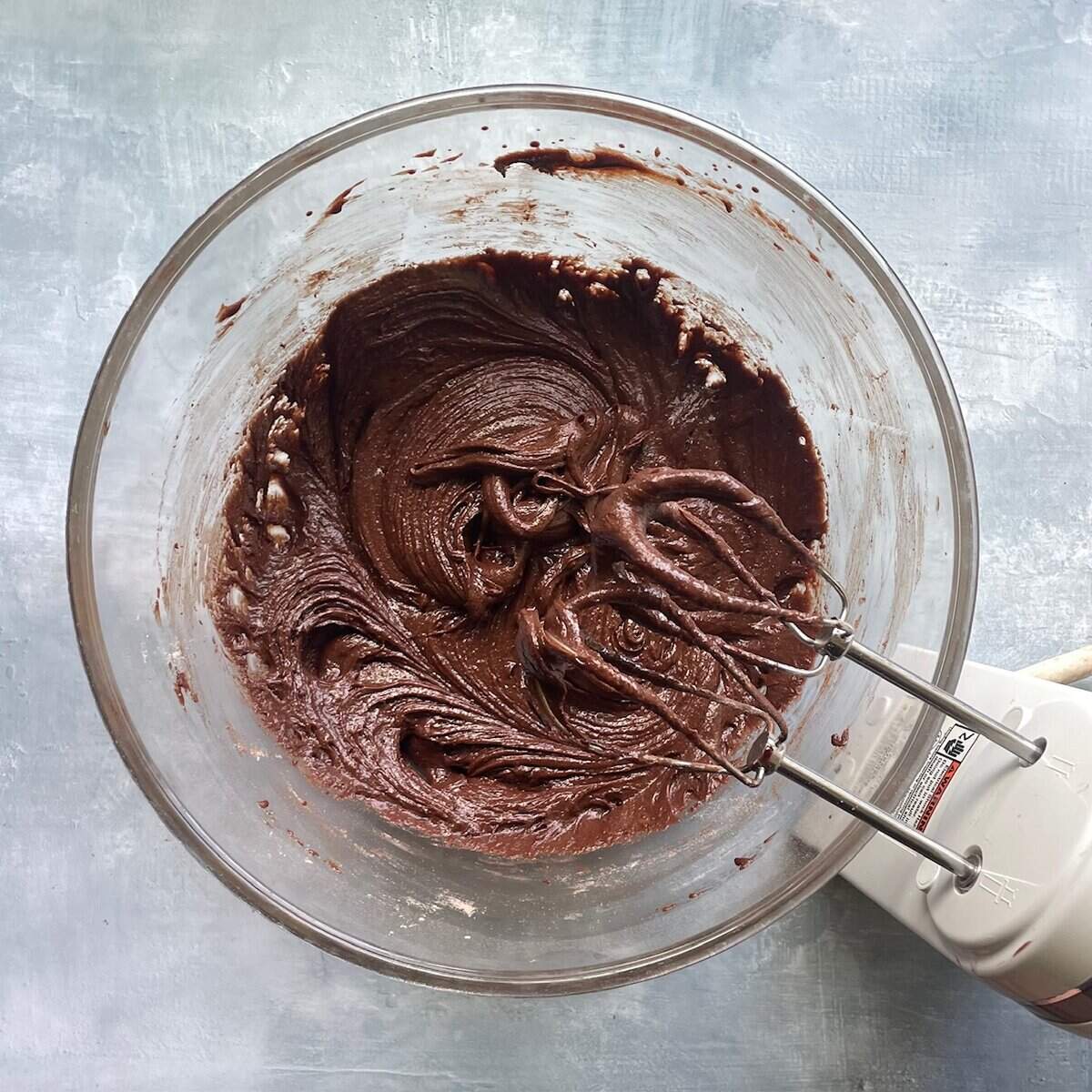 thick chocolate batter in a large glass bowl with handheld beaters.