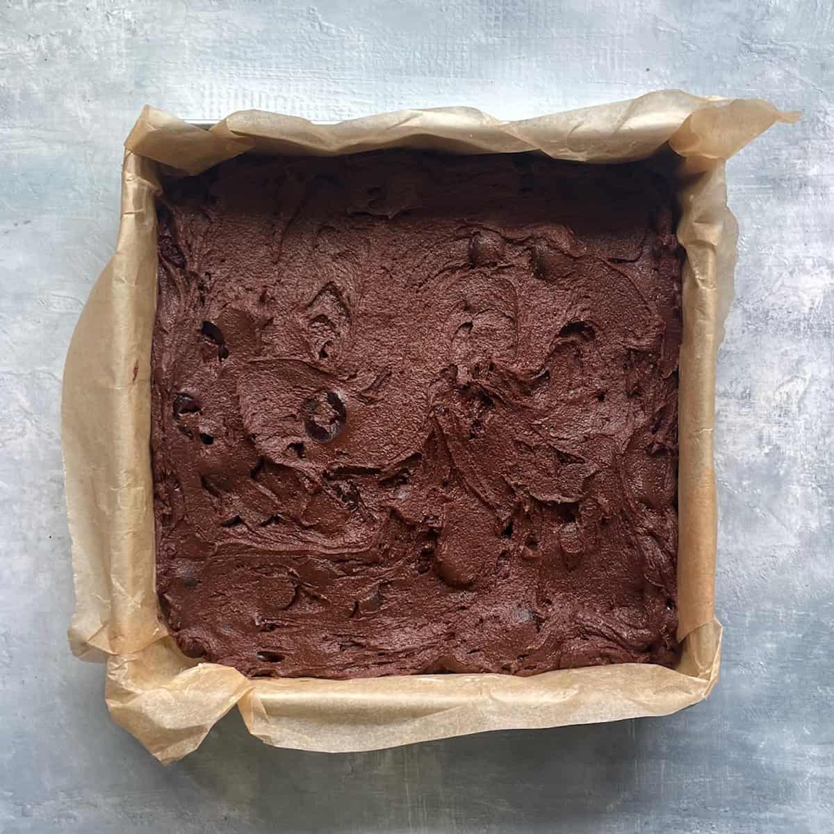 unbaked cherry and chocolate brownie batter in a square baking pan lined with parchment.