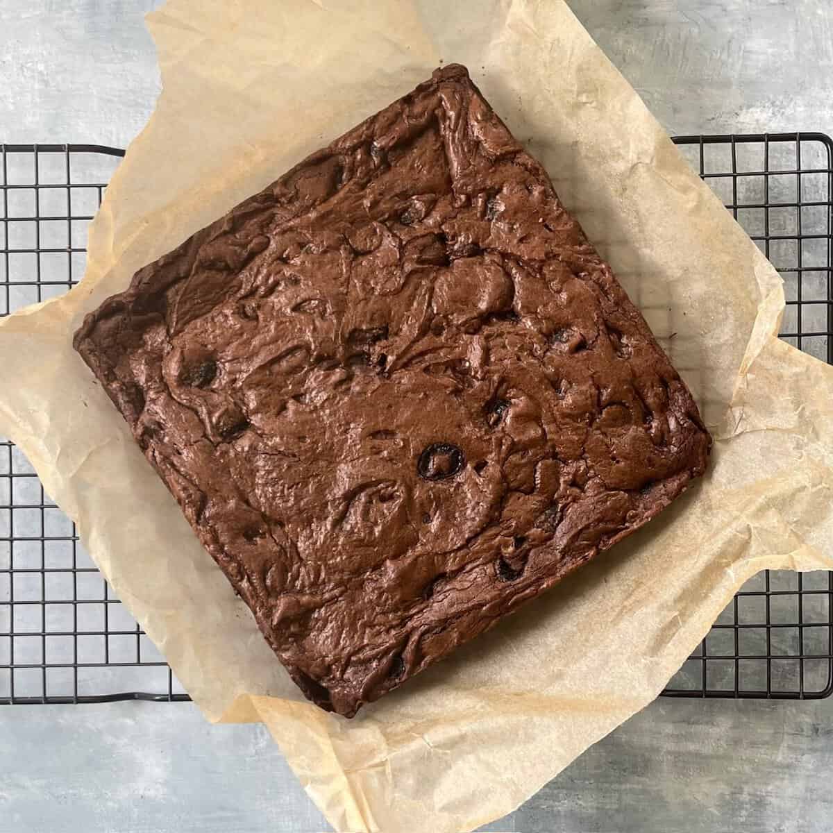 baked cherry brownies on parchment paper on a cooling rack.