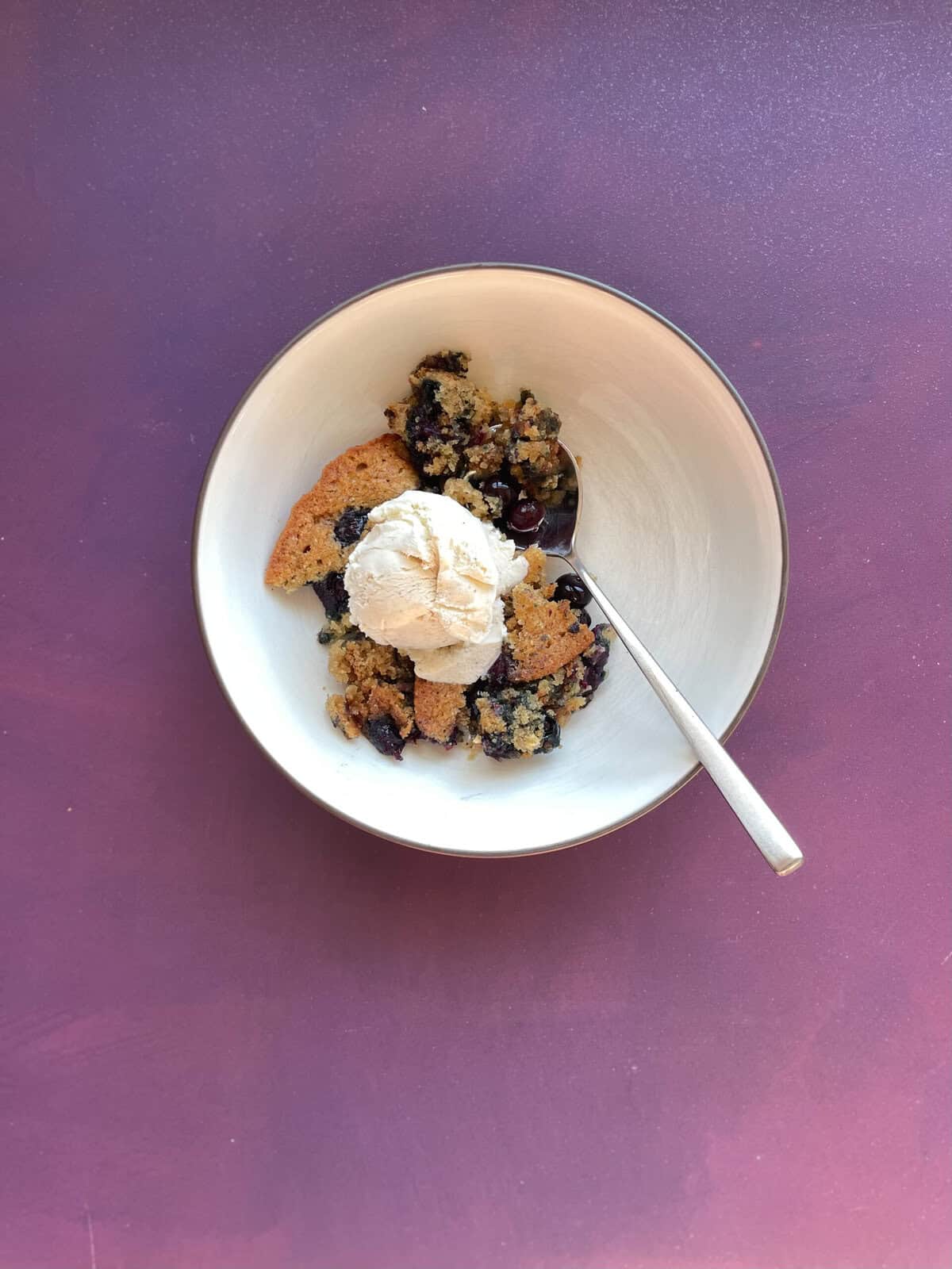 bowl of blueberry spoon cake topped with scoop of vanilla ice cream.