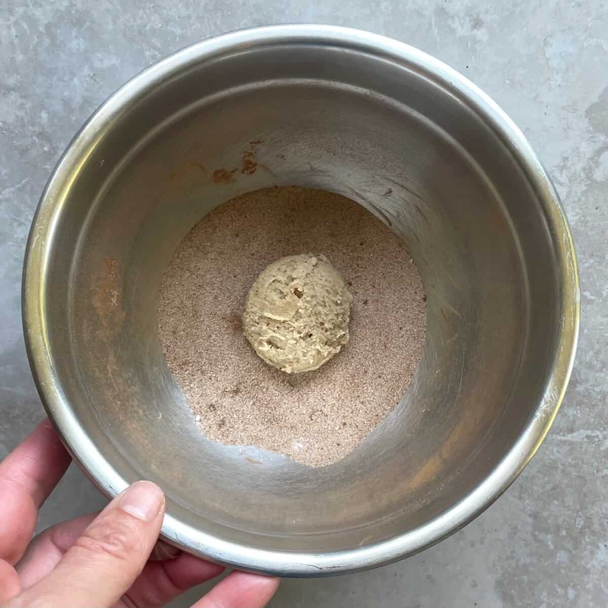 snickerdoodle cookie ball in a metal bowl with cinnamon sugar.