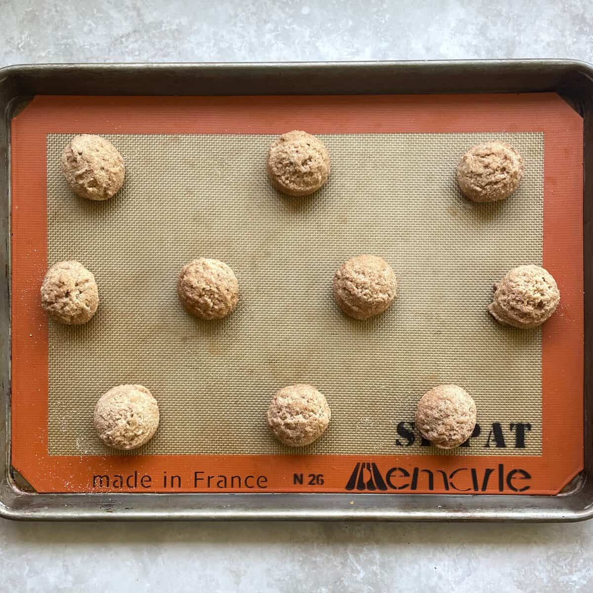 ten unbaked balls of brown butter snickerdoodle cookie dough on a silicone lined baking sheet.