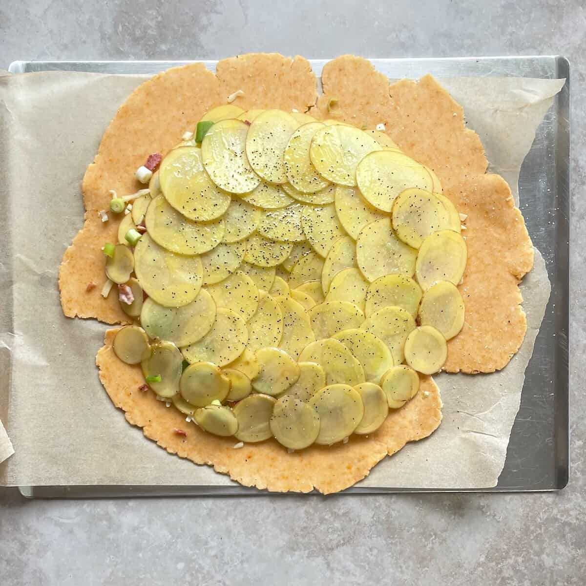 unbaked potato galette with the second layer of overlapping potato slices topped with black pepper.