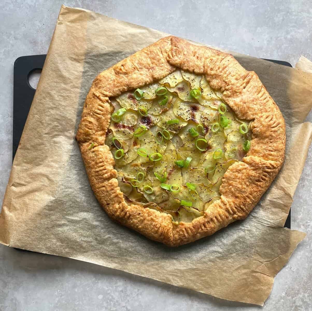 baked potato galette with bacon and green onions on parchment paper.