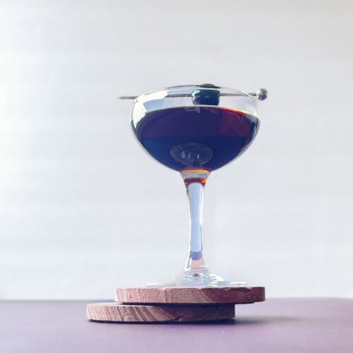 black manhattan in a coupe garnished with luxardo cherry.