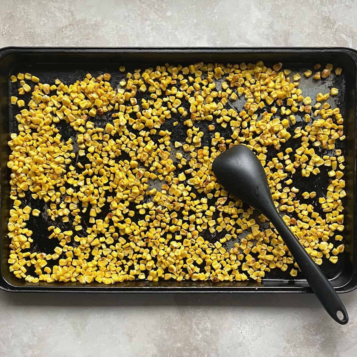 browned corn kernels on a sheet pan with silicone spatula.