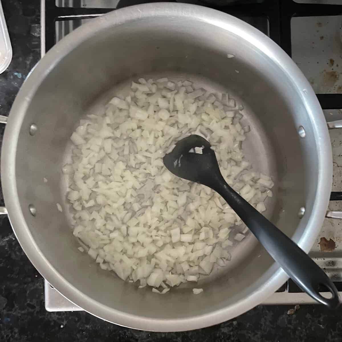 chopped onions in a soup pan with black silicone spatula.