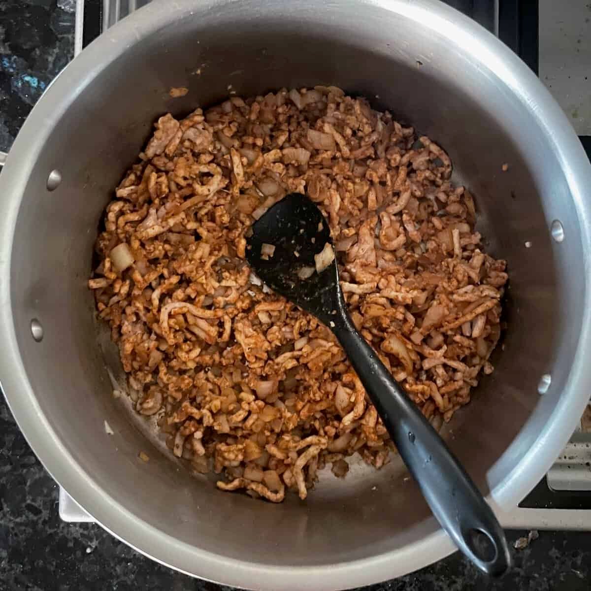 onions and ground chicken in a soup pot with black silicone spatula.