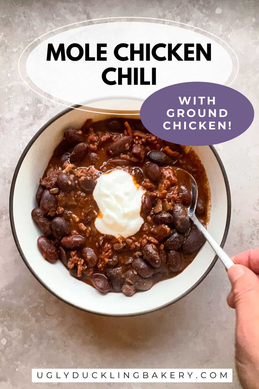 hand holding spoon dipping into a bowl of ground chicken chili. The title says Mole Chicken Chili with Ground Chicken. The website ugly duckling bakery dot com is below.