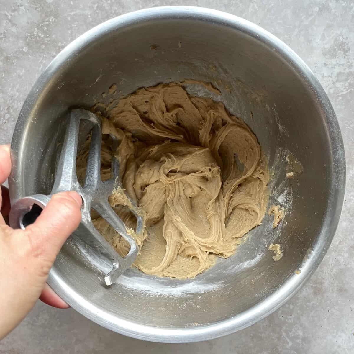 thick brown batter in a mixing bowl with a hand holding a beater.