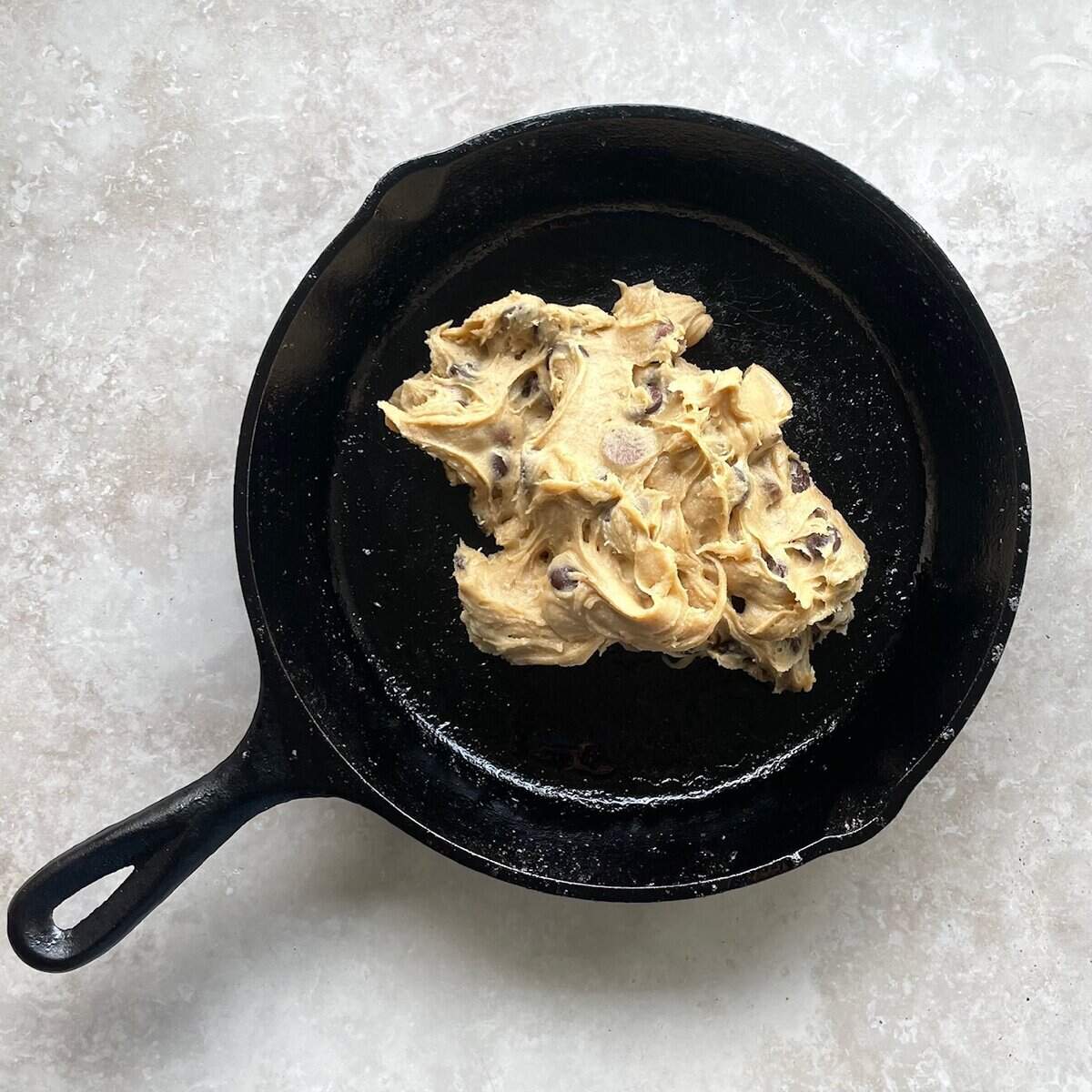 chocolate chip cookie batter dolloped into a cast iron skillet.