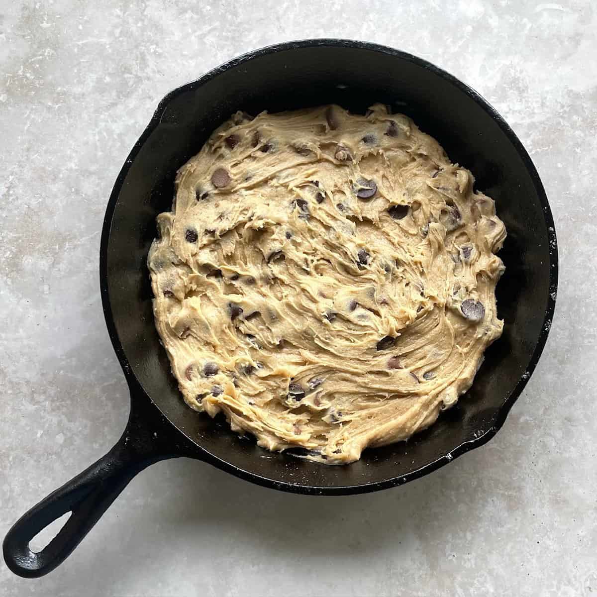 chocolate chip cookie batter spread evenly into a cast iron skillet.