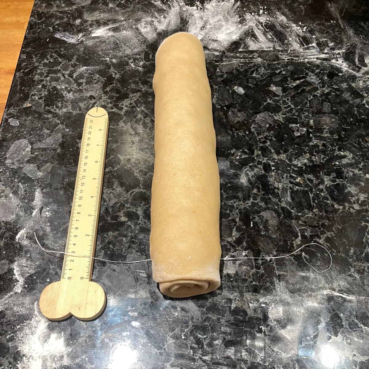 log of cinnamon rolls next to a ruler with a length of dental floss one inch in.