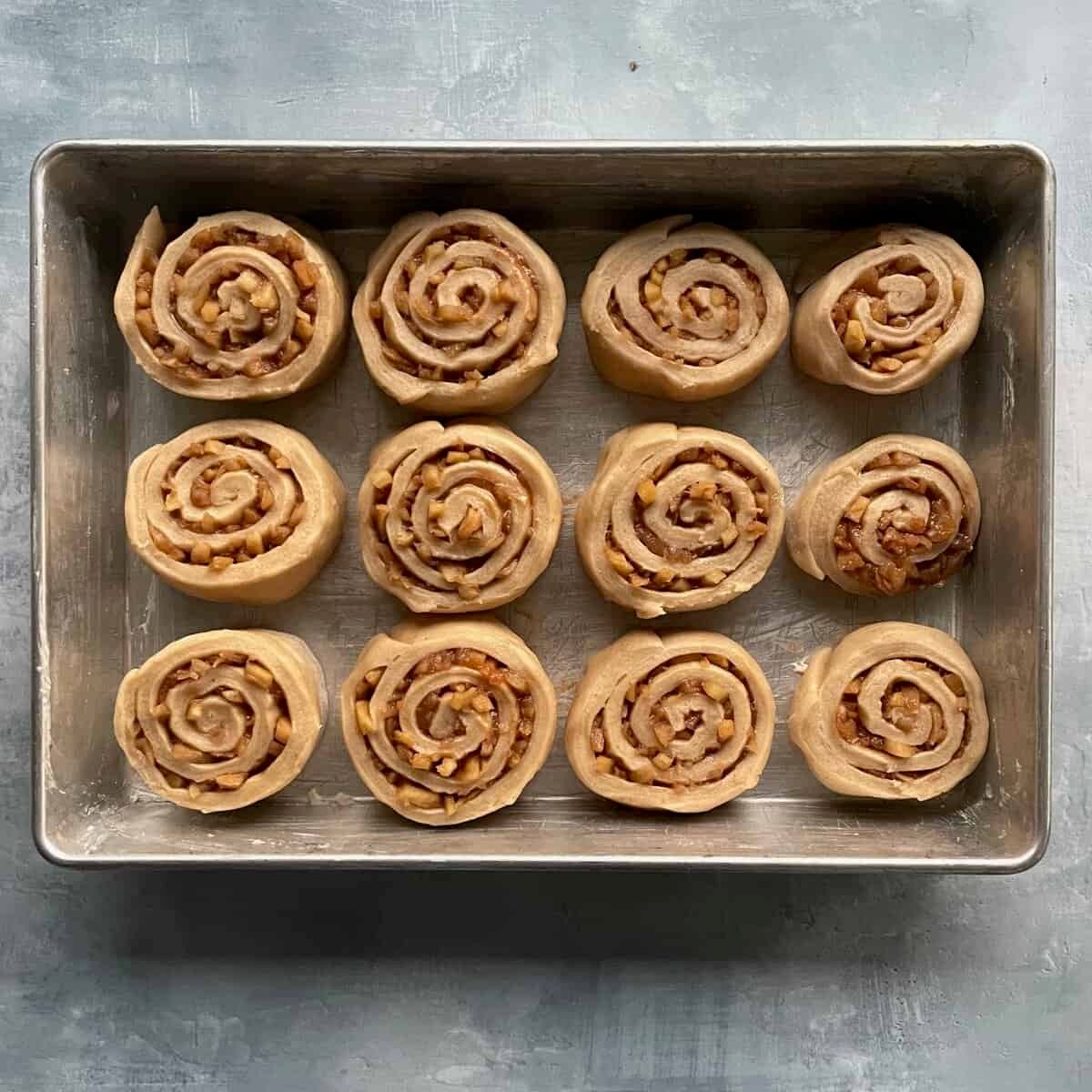 twelve unrisen apple pie cinnamon rolls in a rectangular baking pan.