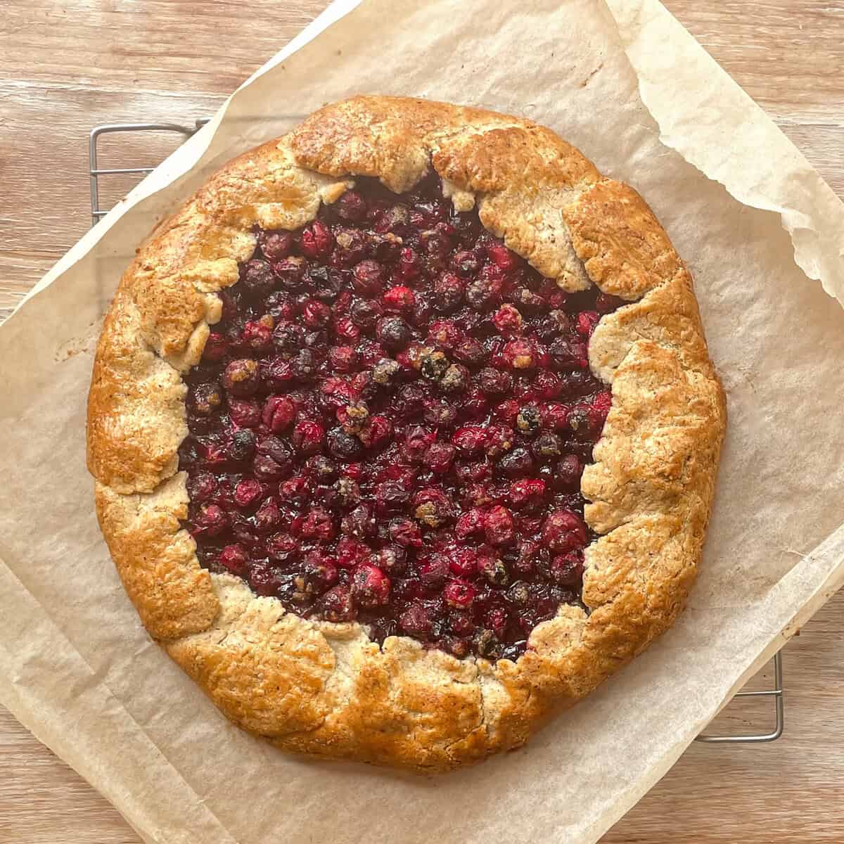 baked cranberry galette with a nut crust on parchment paper on a cooling rack.
