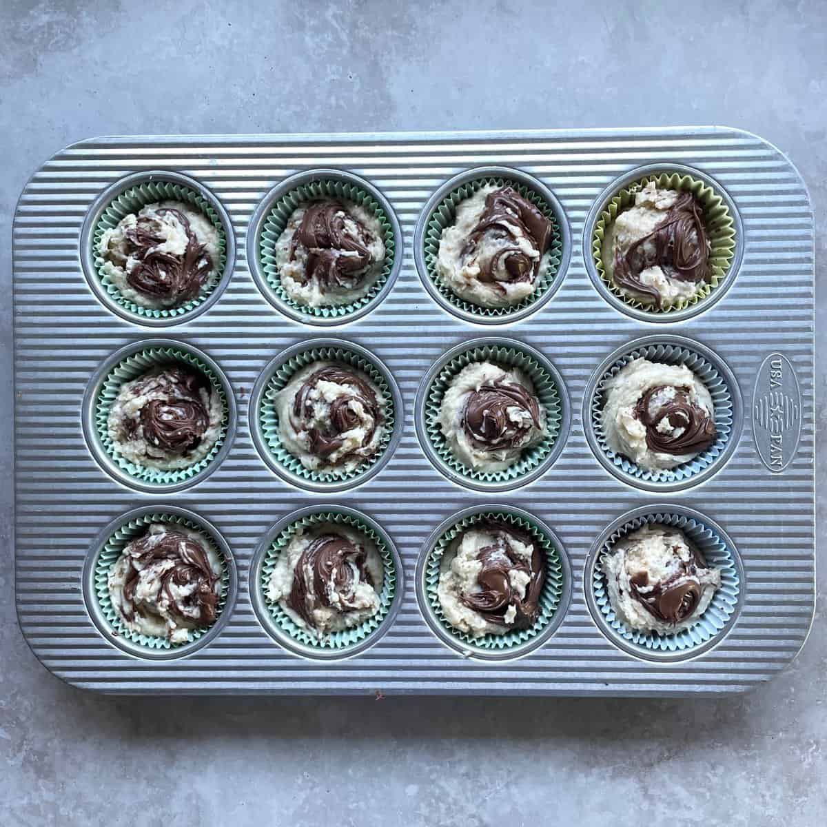 Unbaked Nutella swirl muffins in a lined muffin tin.