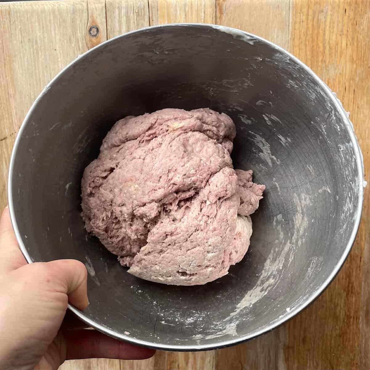ball of pink purple bread dough in a mixing bowl.
