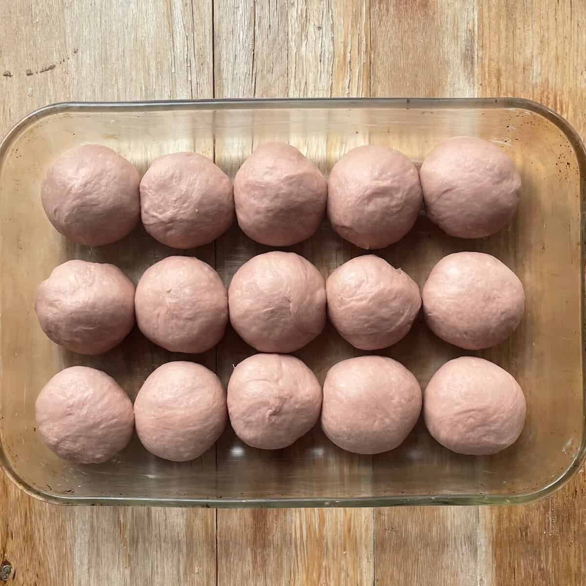 fifteen balls of purple sweet potato bread rolls in a greased glass baking dish before rising.