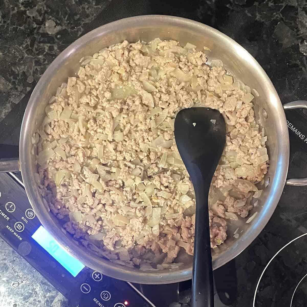 ground chicken, pieces of vegetable, and black silicone spatula in a large skillet on a cooktop.