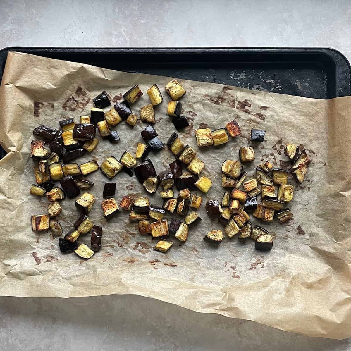 cubes of roasted eggplant on parchment paper on a baking sheet.