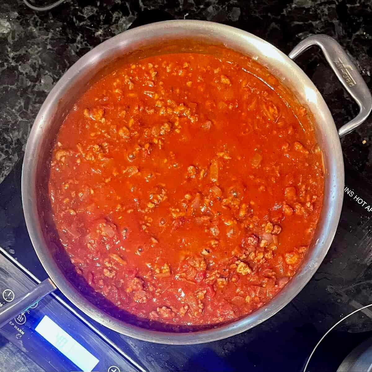 large frying pan on the cooktop filled with a tomato sauce with ground chicken.