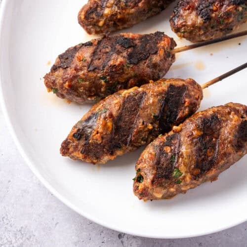 grilled beef kofta kebabs on skewers on a white platter.