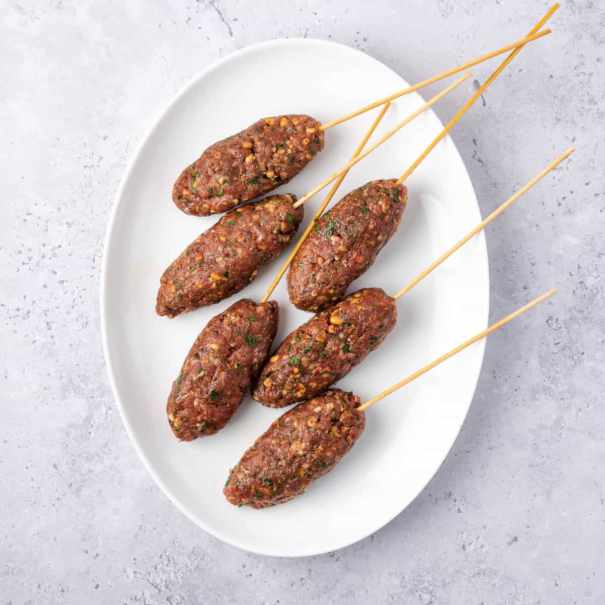 beef kofta mixture shaped into six logs with a skewer inserted through the middle of each.