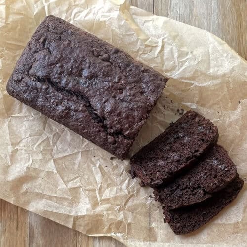 sliced chocolate loaf cake with chocolate chips on a crinkled piece of parchment paper.