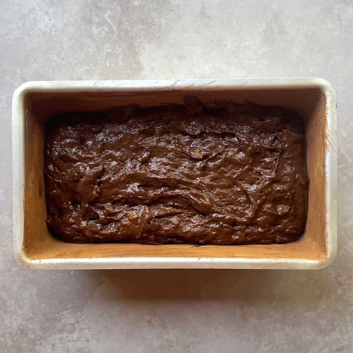 unbaked chocolate chocolate chip loaf cake in a cocoa dusted loaf pan.