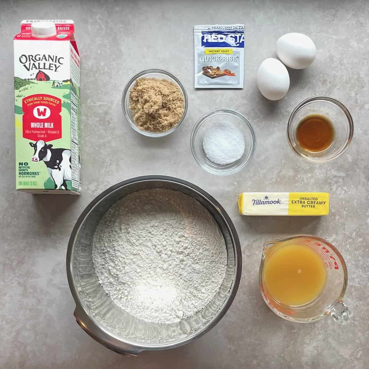 carton of milk, stick of butter, two eggs, packet of yeast, and bowls of brown sugar, flour, pineapple juice, vanilla, and salt.