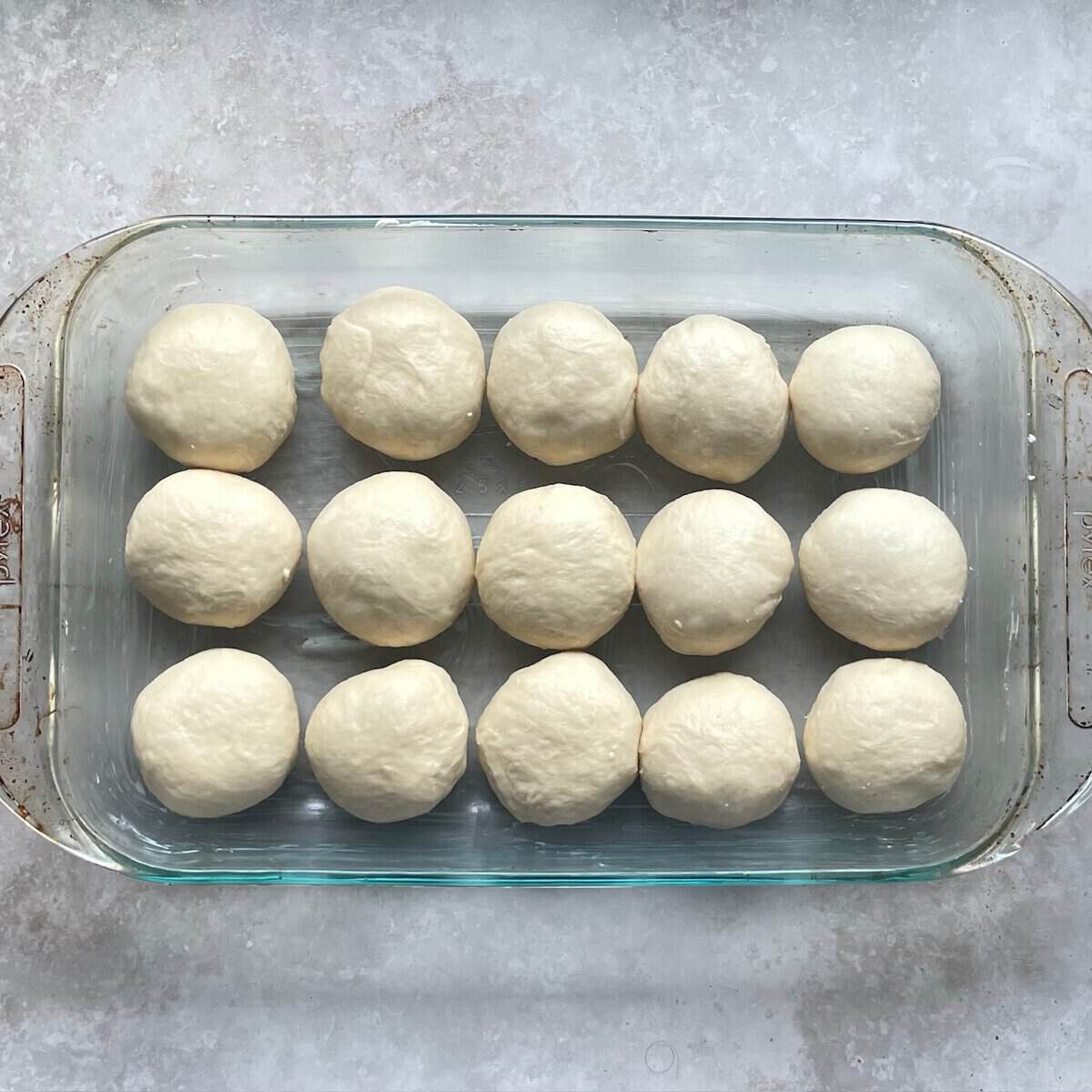 fifteen dinner rolls arranged in three rows of five rolls in a glass baking dish.